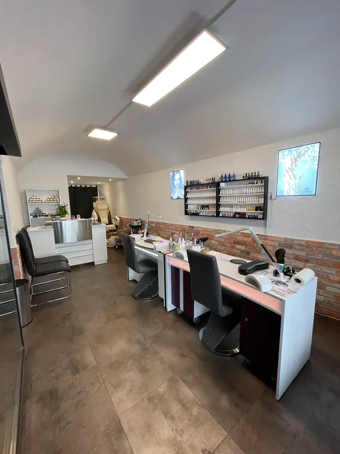 Innenraum von Le Nails mit Gewölbedecke, Backsteinwand, Nageltischen und einem Regal voller Lackfarben